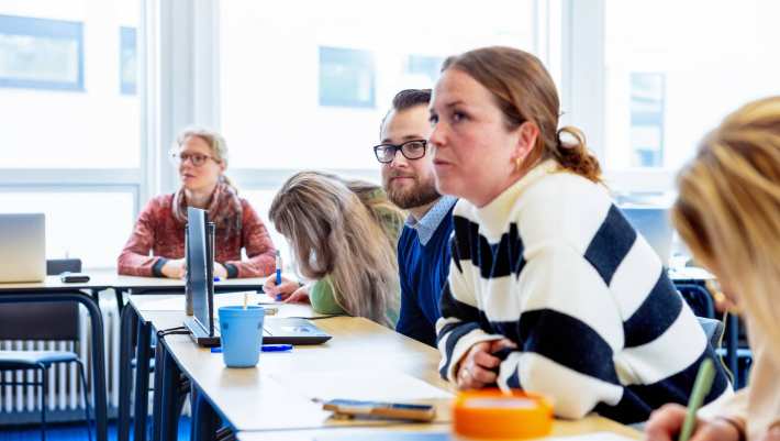 Vrouw met witte trui met zwarte strepen luistert naar presentatie. Op de groenewoudseweg, opleiding maag-, lever,- darmverpleegkundige.