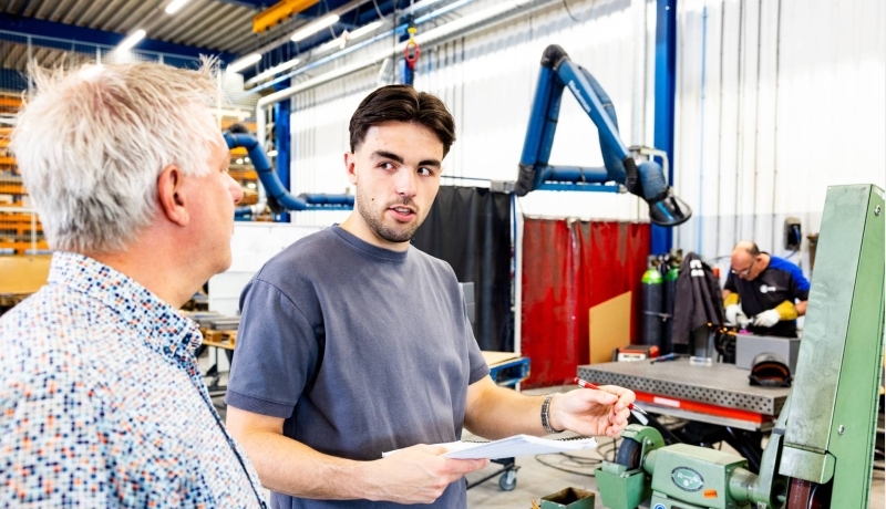 Technische Bedrijfskunde student overlegt met stagebegeleider bij machine.