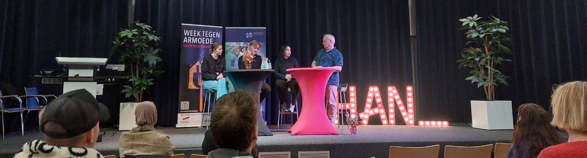 sfeerbeeld van de opening van de week tegen armoede. Mensen zitten op een stoel in een zaal met rode vloerbedekking.