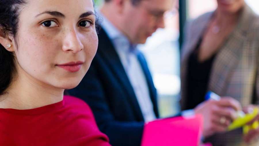 Beeldmerk voor het project ALL4TALENT. Een vrouw houdt een post-it omhoog en kijkt de camera in.