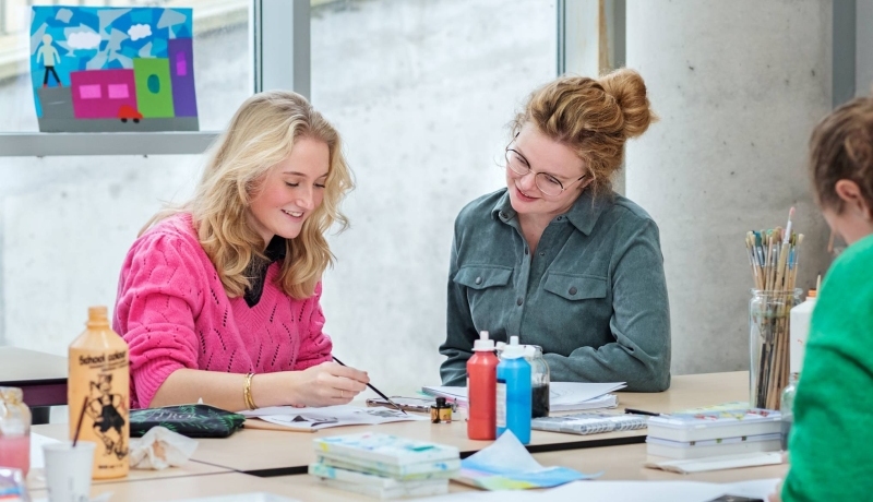 Fotoshoot maakdagen beeldende vorming 2022. Docente kijkt mee met studente tijdens het schilderen
