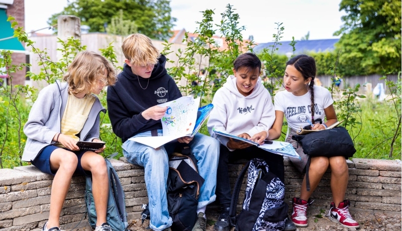 Vier leerlingen lezen buiten op een bankje. Foto van de opleiding leraar basisonderwijs