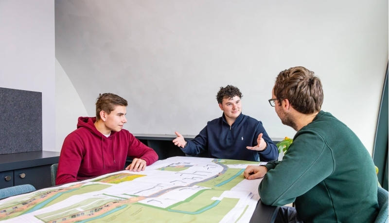 drie mannen in een overlegsituatie met een omgevingskaart op de overlegtafel