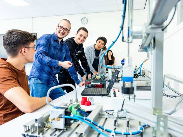 Docent en studenten elektrotechniek  aan een Programmable Logic Controller (PLC).