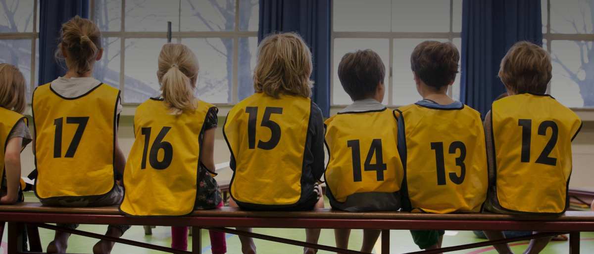 Kinderen in een gymzaal met hesjes aan op de rug gefotografeerd