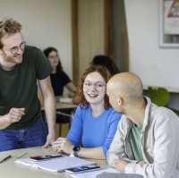 Leraar Wiskunde luistert lachend naar zijn twee studenten die iets zeggen tegen hem