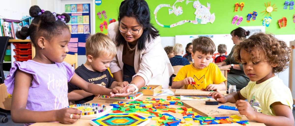 De kinderen in de klas leggen een puzzel en de lerares van de opleiding leraar basisonderwijs helpt hen hierbij.