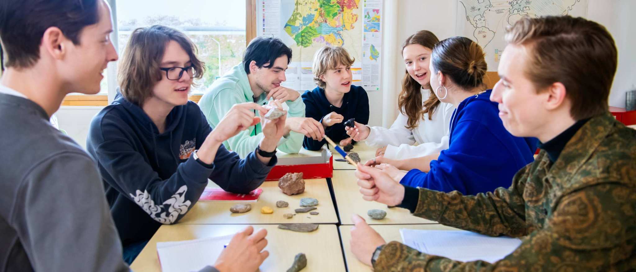 Studenten overleggen samen aan tafel in de klas. 