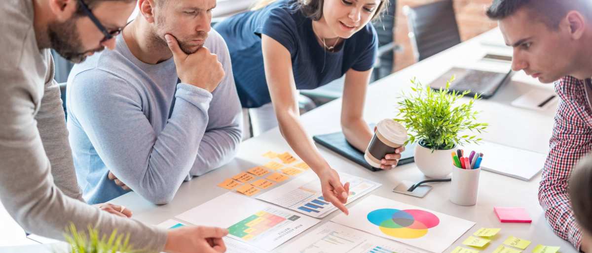 Sfeerbeeld van collega's die samenwerken aan een tafel met post-its, schema's en tabellen 