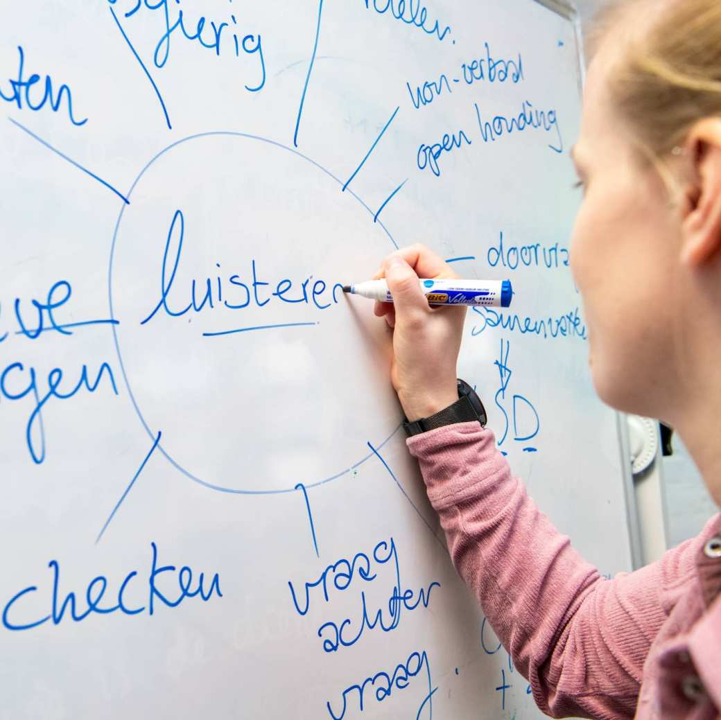 Vrouw met paardenstaart schrijft op een whiteboard.