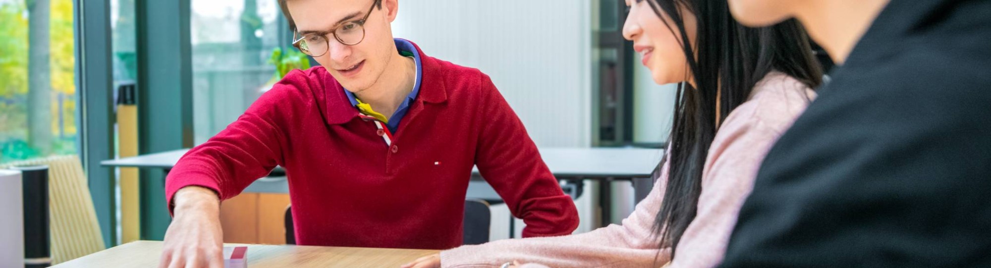 Drie mensen zitten aan tafel en kijken naar gekleurde kaartjes die gesorteerd op tafel liggen