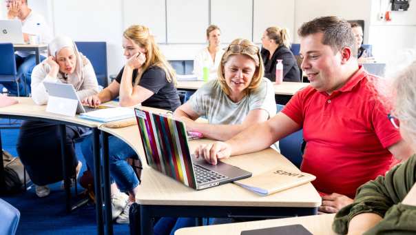 Docent kijkt mee met student die een rood shirt aan heeft