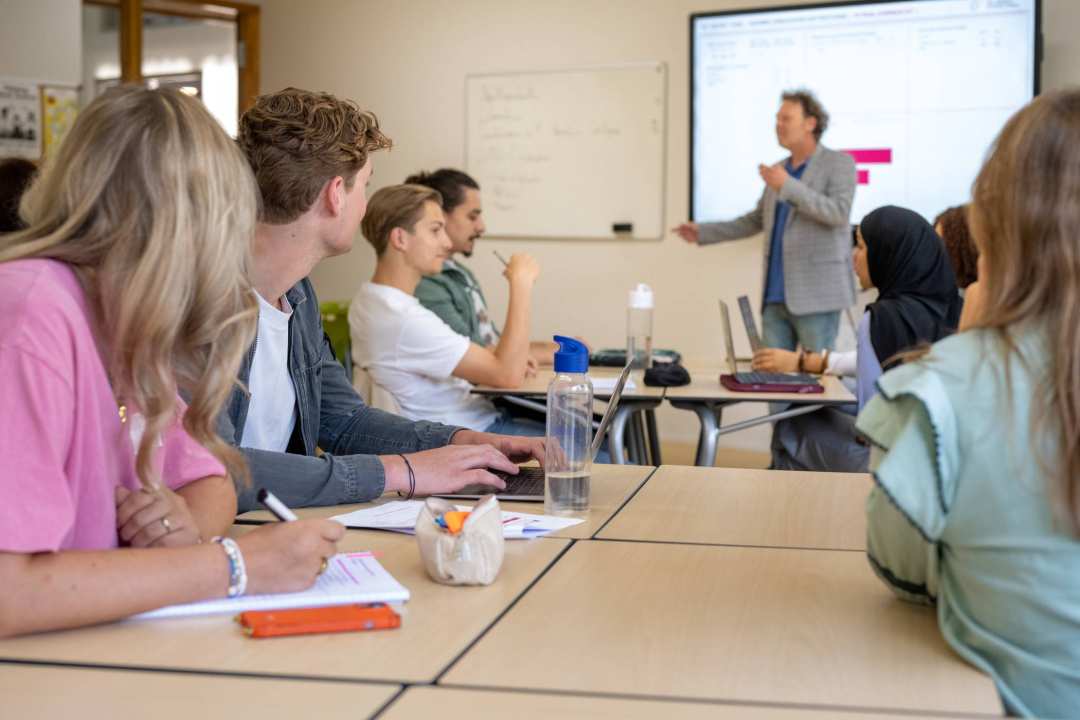 Studenten in een klas die luisteren naar de uitleg van een docent. 