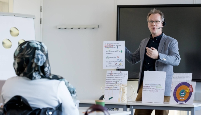 Man houdt presentatie en houdt hierbij ideeën op papier in de lucht voor de klas