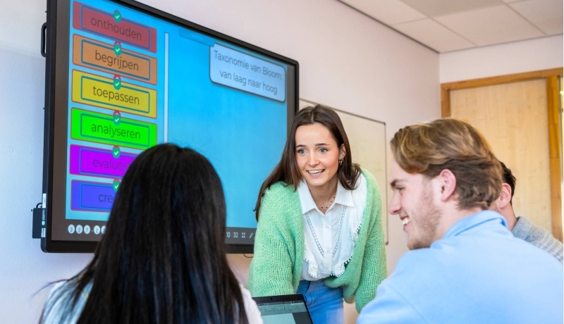 Studenten van Leraar Economie werken aan een groepsopdracht en de docent kijkt toe.