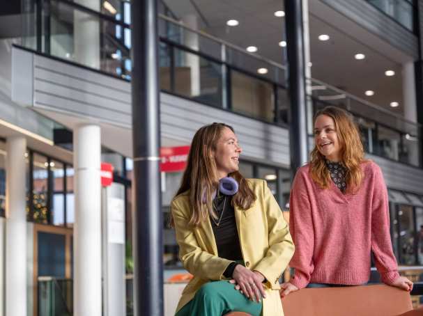 2 studenten staan en zitten in een hal.