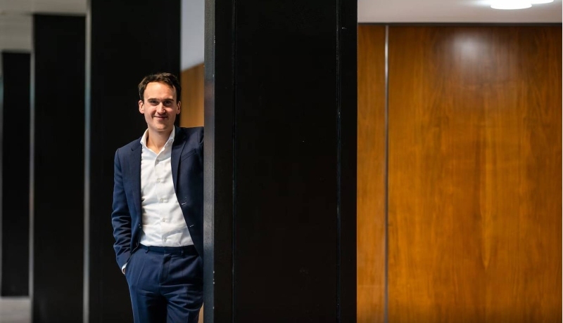 foto van spreker/wethouder in een donkerblauw pak met wit hemd, leunend tegen een muurtje