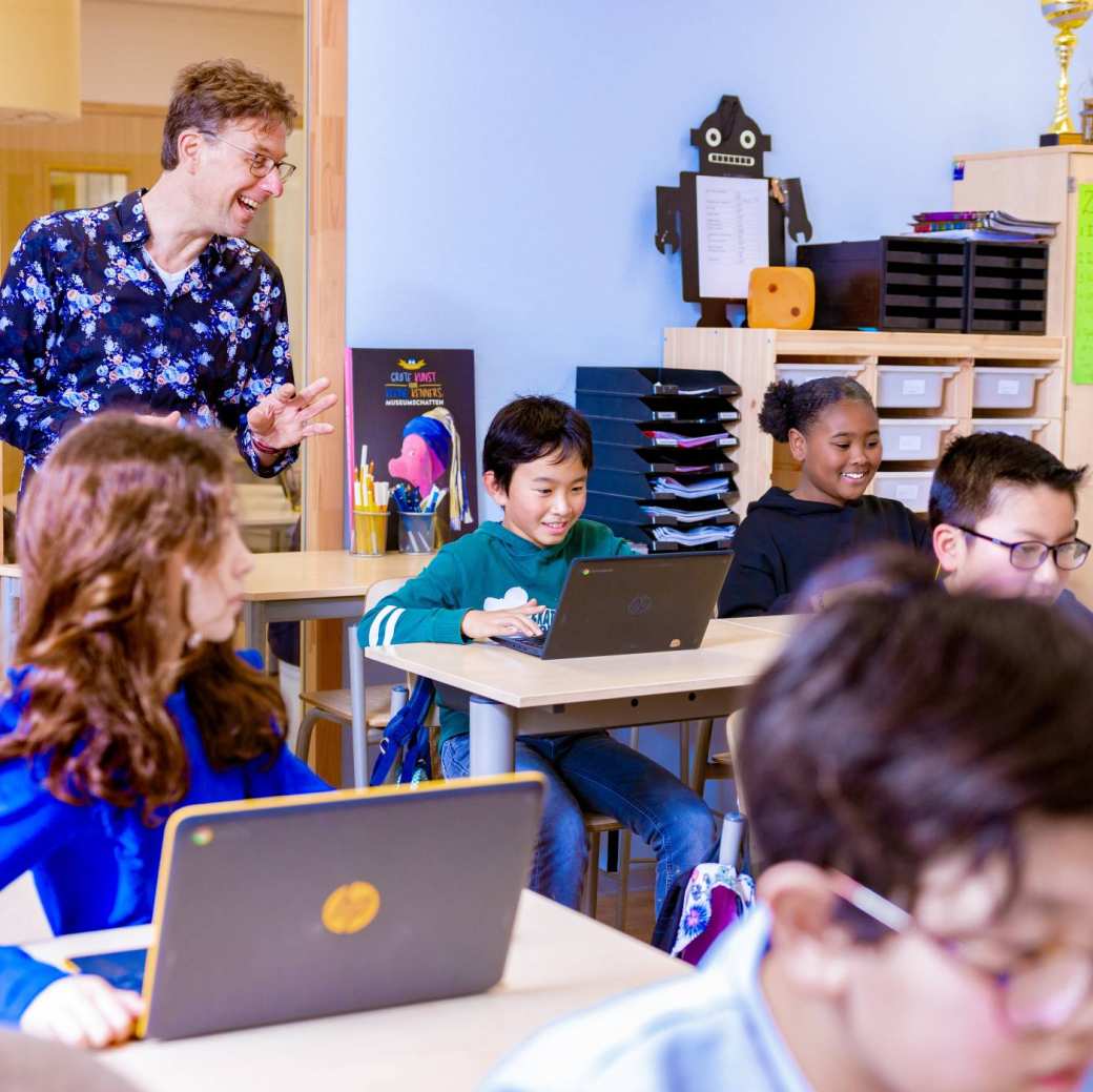 Groep 5,6,7 op de school Da Vince. De leraar praat tegen de leerlingen in de klas achter de laptop.
