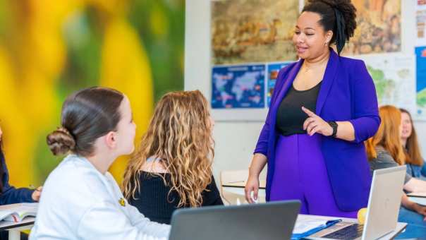 Twee studenten luisteren naar docent en kijken haar aan