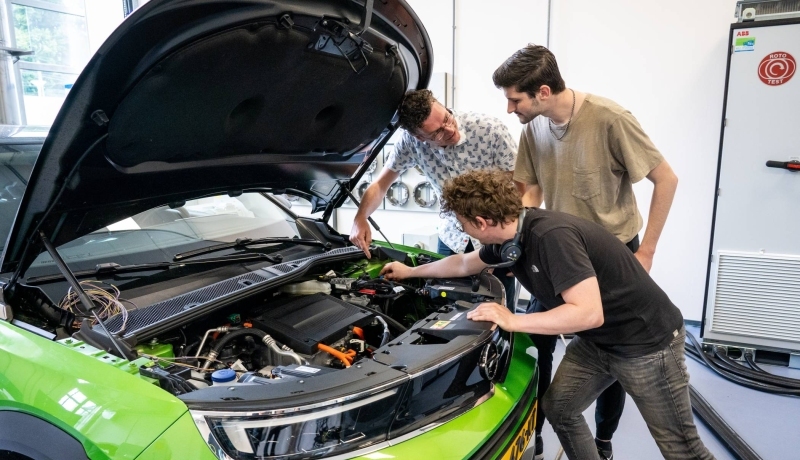 Studenten en docent automotive kijken naar de motor van de auto.