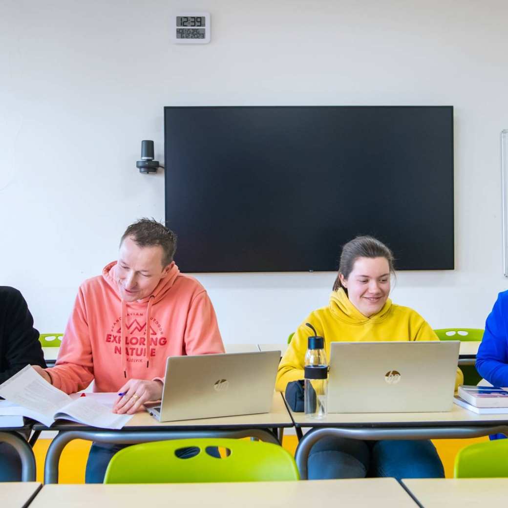 Foto Master Academie Educatie. 4 masterstudenten zitten geconcentreerd op een rij achter hun laptops aan een tafel.