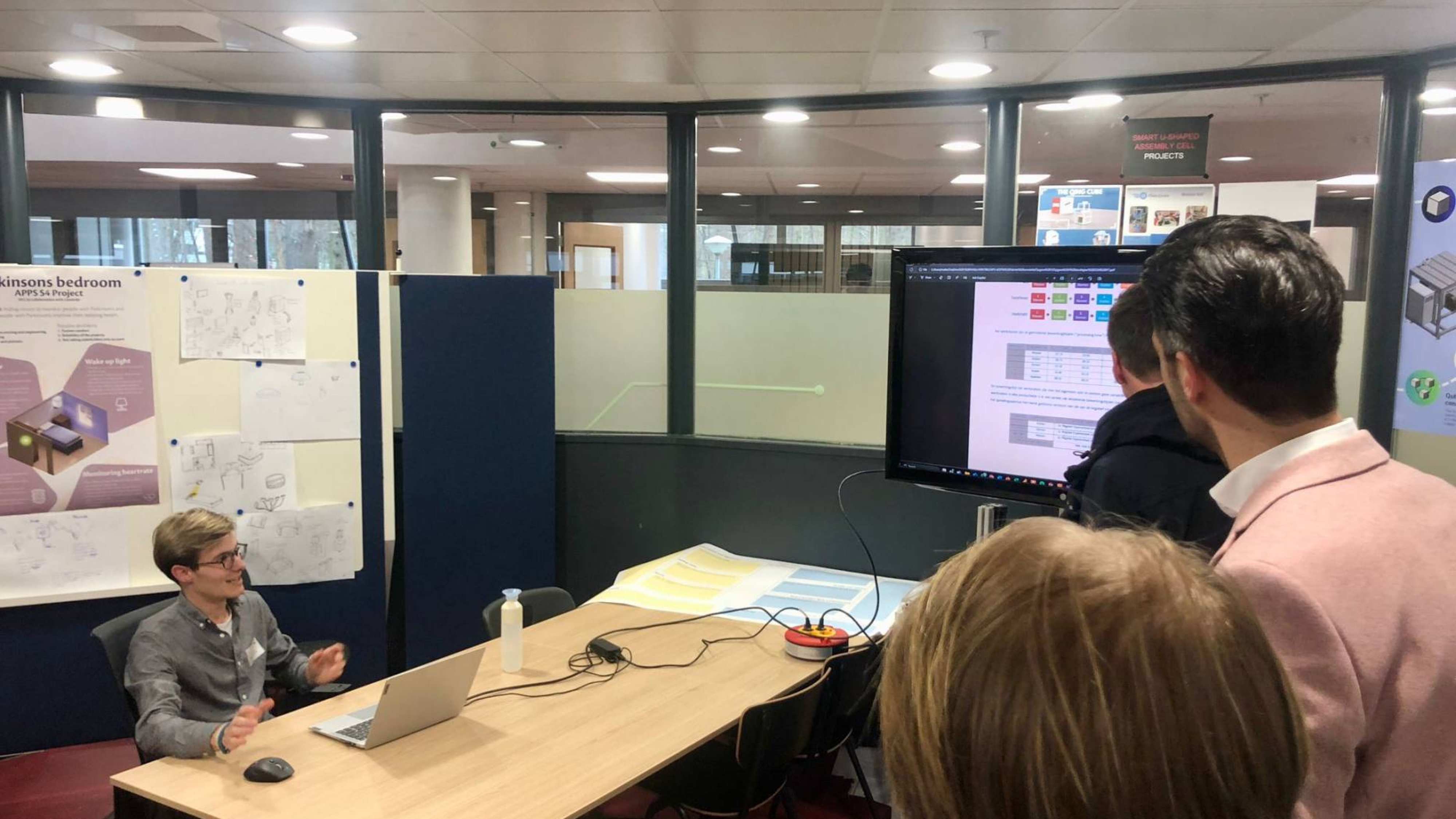 Een student zit aan een tafel en presenteert zijn project tijdens de accreditatie