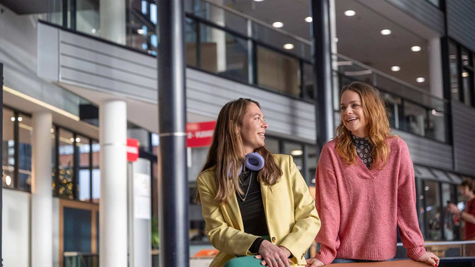 2 studenten staan en zitten in een hal.