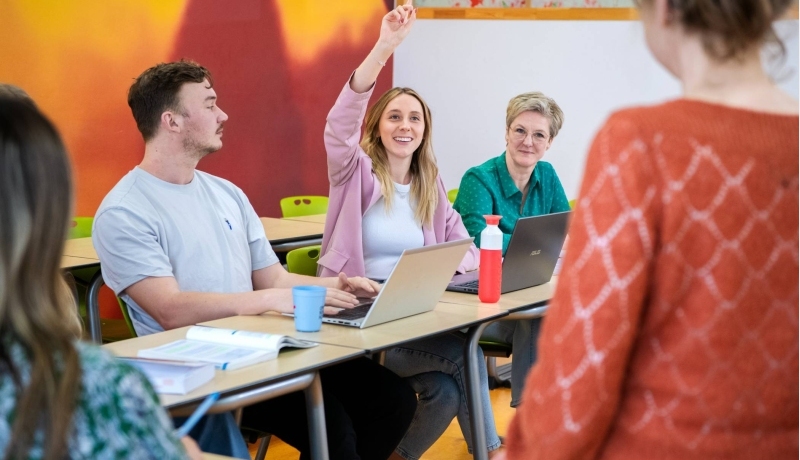 Drie master studentes zitten lachend aan tafel.