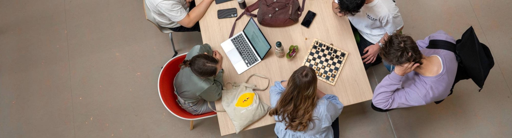 Studenten zijn aan het werk, aan een tafel, foto van bovenaf genomen. 
