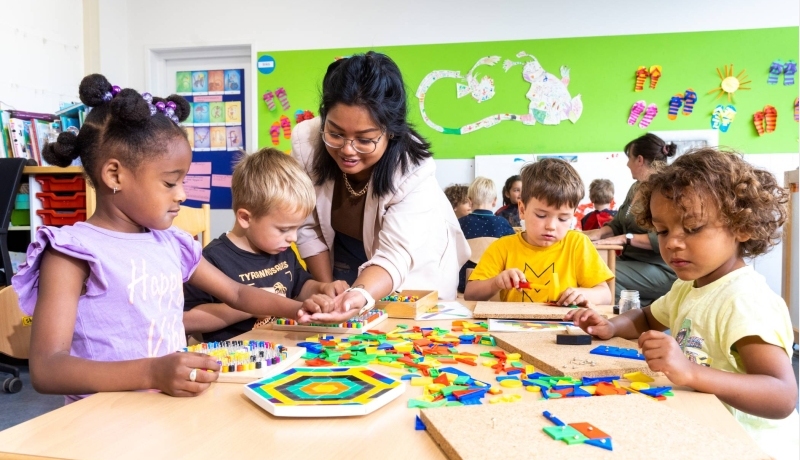 De kinderen in de klas leggen een puzzel en de lerares van de opleiding leraar basisonderwijs helpt hen hierbij.