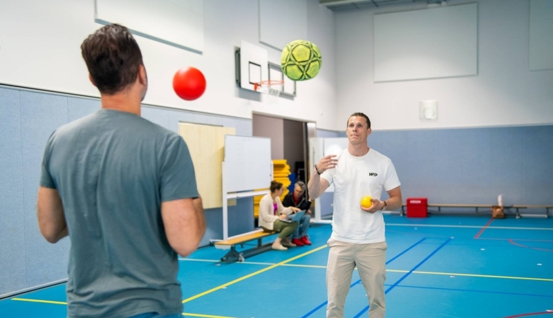 Twee studenten die ballen overgooien tijdens les PMT deeltijd
