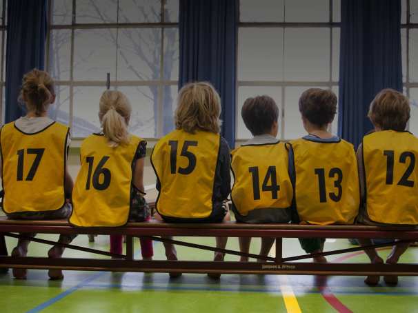 Kinderen in een gymzaal met hesjes aan op de rug gefotografeerd