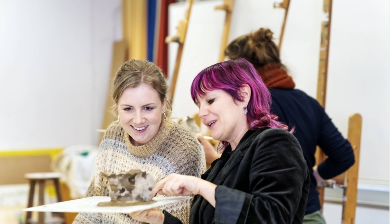 2 studenten van de han master vaktherapie beeldende therapie kijken naar een werkstuk tijdens een les boetseren
