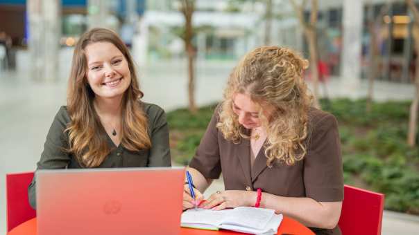 Twee studenten lachen en aan het werk op het vlak van digitale toegankelijkheid achter de laptop