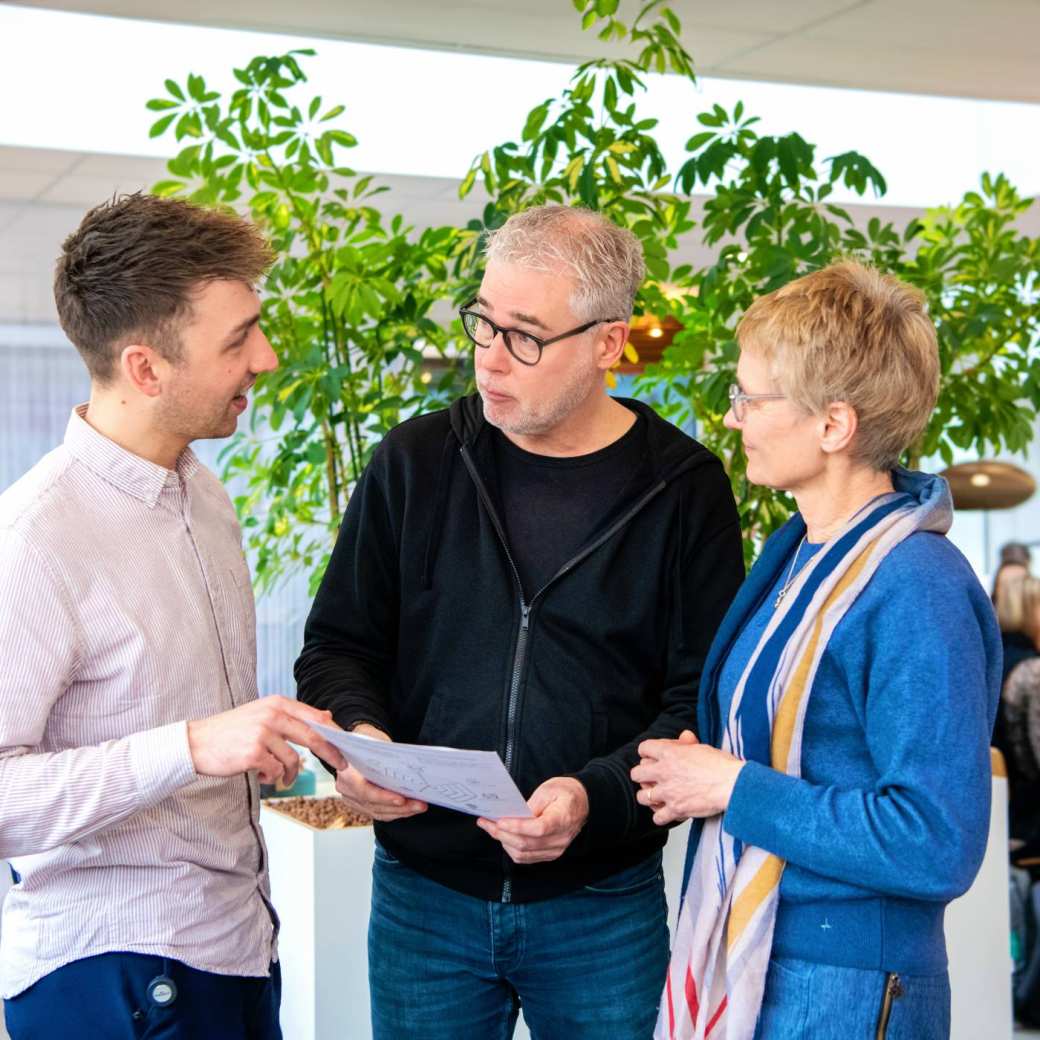 Student praat met docenten terwijl hij een blad vasthoudt.
