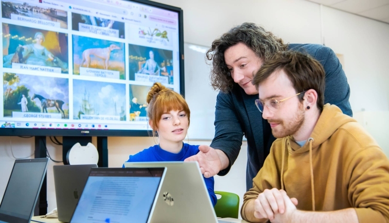 Twee studenten lachen met elkaar tijdens het werken achter de laptop.