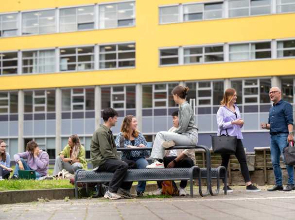 Studenten zijn buiten, zitten aan picknicktafel en in het gras. Buiten op campusterrein Arnhem.