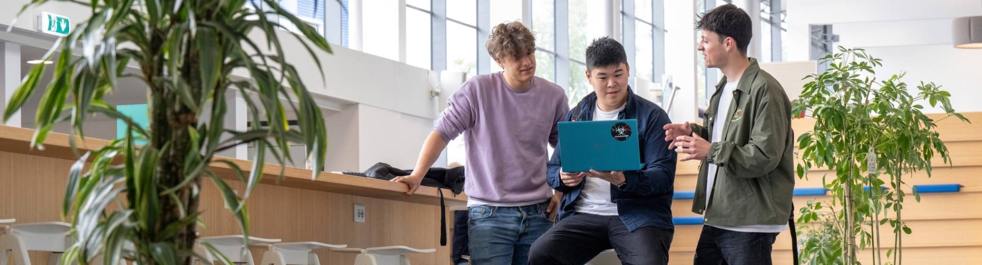 Drie jongens staan in de hal en kijken samen op een telefoon, uitgezoomde foto. 