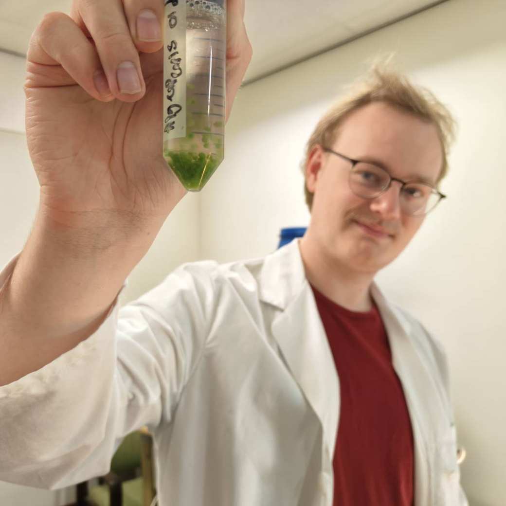 Bas Emaus, blond haar, brilletje op, in een labjas met zijn algenparels in zijn hand