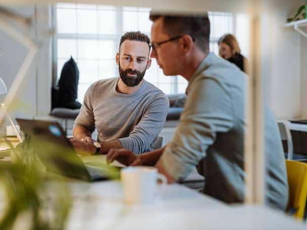 Twee mannen zitten aan een bureau en zijn in overleg in een kantoorruimte.