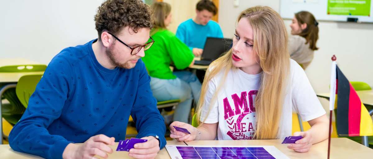Twee studenten spelen een kaartspel met blauwe kaartjes in een gekleurd leraar Duits lokaal.