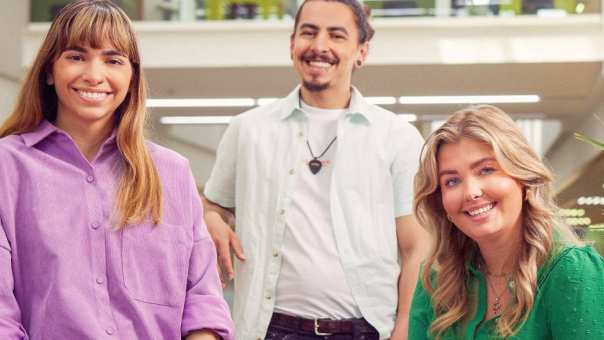 werving voltijd campagne, drie studenten kijken recht in de camera. de jongeman staand, twee jongedames zittend op een tafeltje.