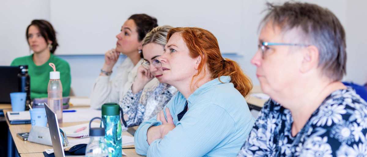 Vijf vrouwen in klaslokaal luisteren naar uitleg docent bij de opleiding technische thuiszorgverpleegkundige.