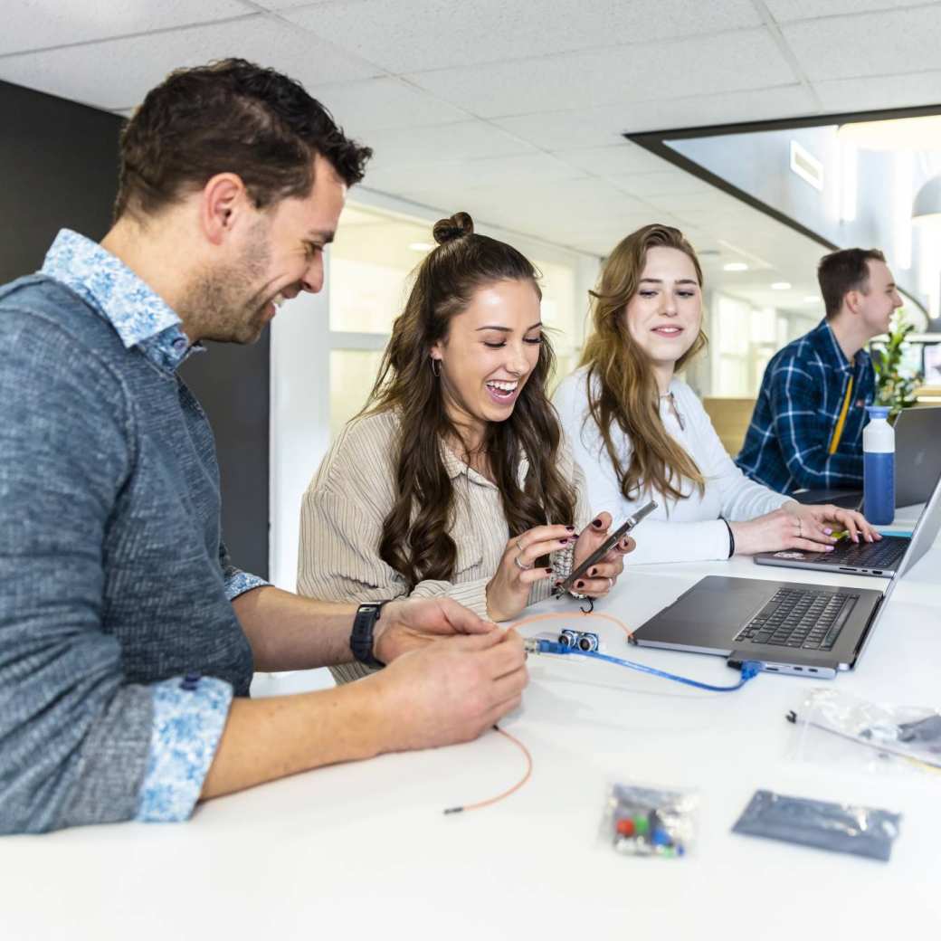 Docent en studenten cmd in overleg met prototype, lachend. 
