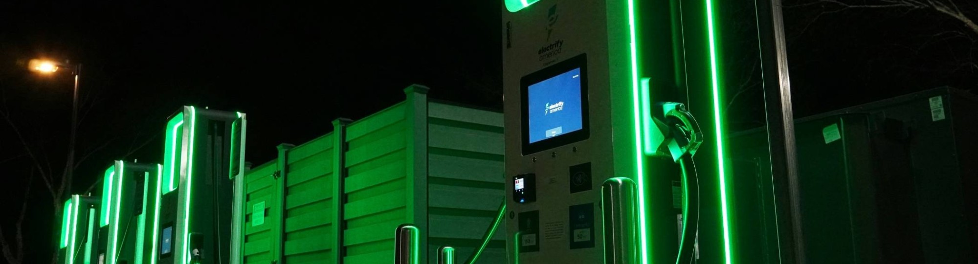 Foto met daarop groen verlicht elektrisch laadstation. Op een van de units staat electrify america