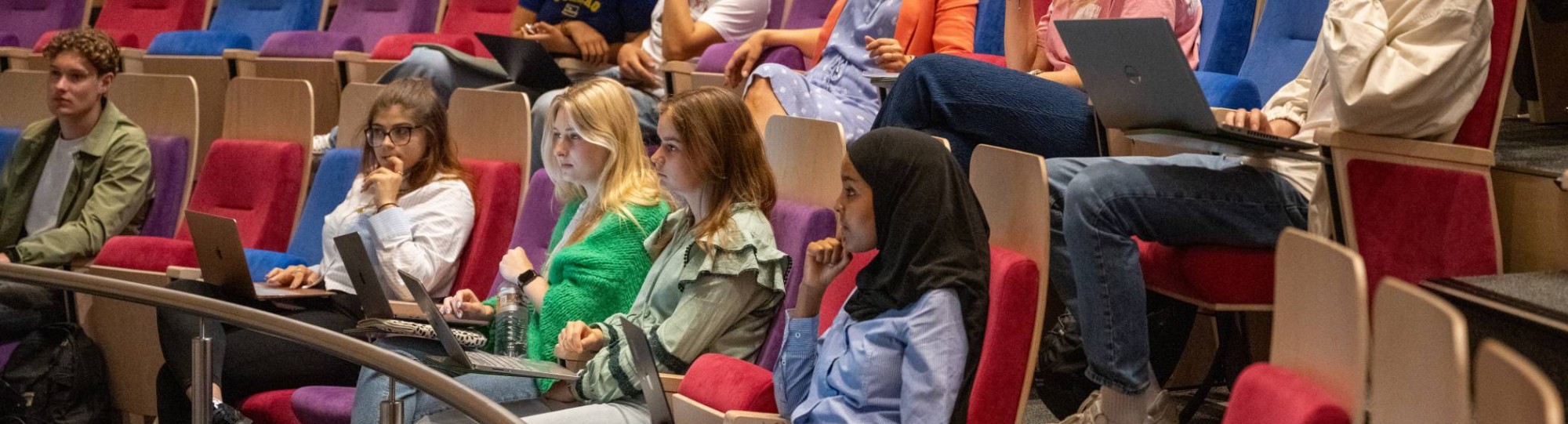 Grote groep studenten zitten in de collegezaal en luisteren naar hoorcollege.
