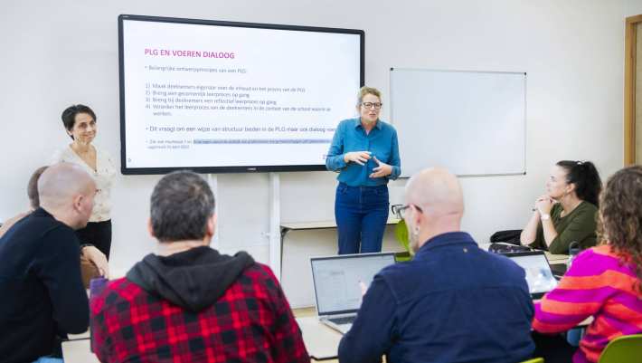 Twee vrouwelijke docenten staan enthousiast uit te leggen voor de klas, terwijl de studenten aandachtig luisteren
