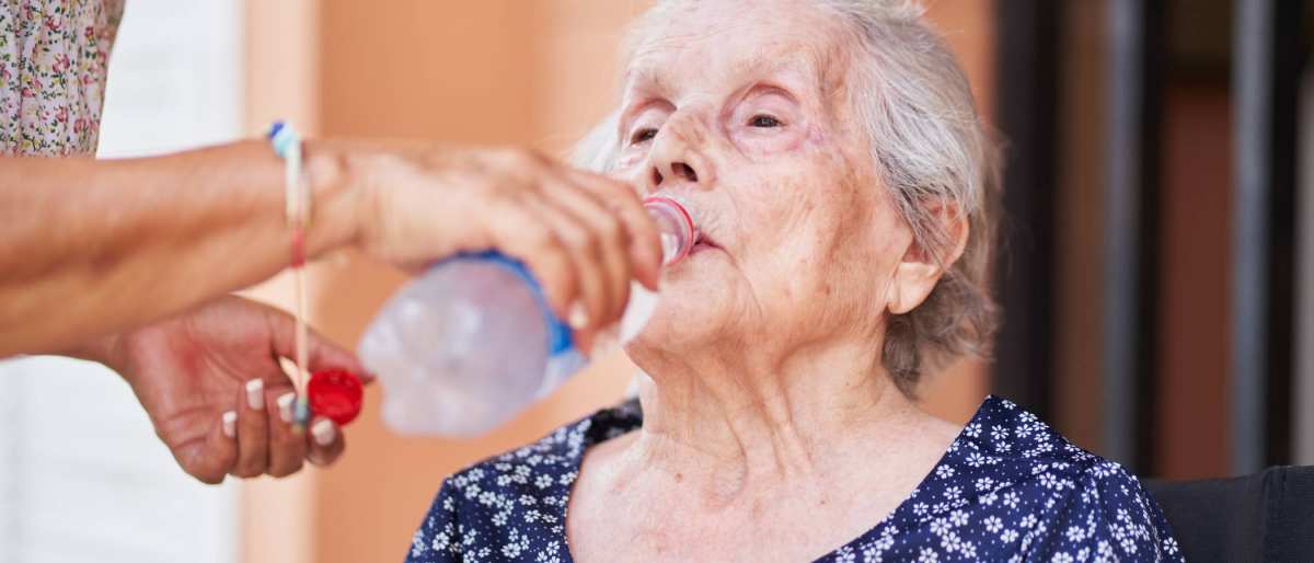 Een oude vrouw drinkt uit een flesje.
