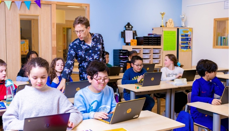 Groep 5,6,7 op de school Da Vince. De leerlingen zitten in de klas achter de laptop terwijl de leraar rond loopt.