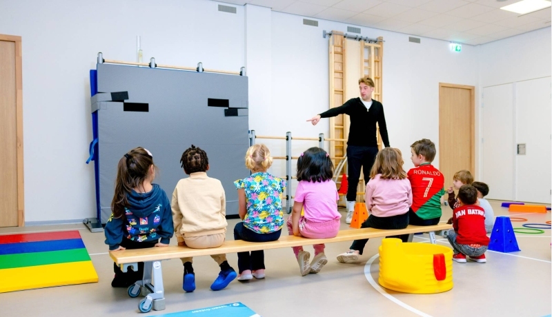 Juf begeleidt kinderen van de glijbaan in de buitenlucht.